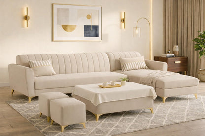 A modern beige sectional sofa with a chaise lounge and matching ottomans in a bright, contemporary living room. The sofa features vertical channel tufting on the backrest and is supported by slim gold-toned legs, set on a patterned rug with a matching coffee table and throw blanket.